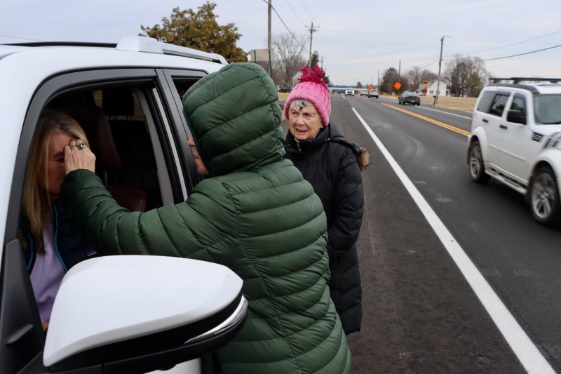 Terry Wilkinson of Lewes, left, receives ashes from Kim Raynes, while Fay Burnham looks on and cars rush by.